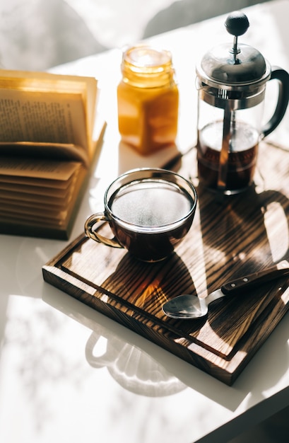 Café préparé dans une presse française et une tasse sur une planche de bois avec un livre ouvert sur une table.