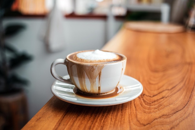 Le café renversé avec du lait dans une tasse blanche ou un cappuccino déborde de la tasse à café sur du bois