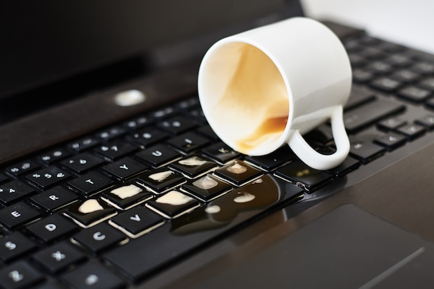 Café renversé d'une tasse blanche sur le clavier de l'ordinateur