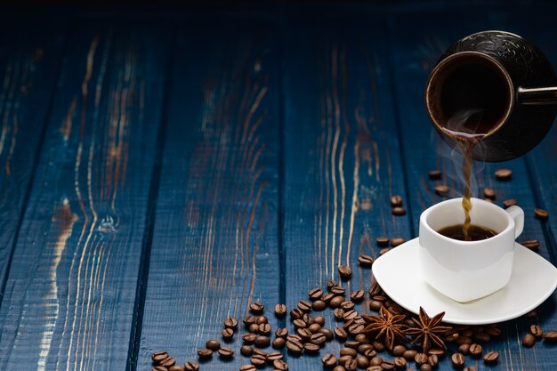 Le café se déverse dans une tasse sur une table en bois bleue avec des grains de café.