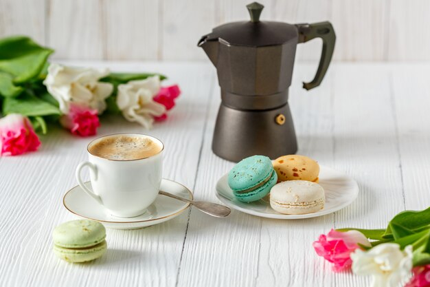 Café, tulipes roses et blanches et macarons sur la table en bois blanche. Petit-déjeuner. Pause café.