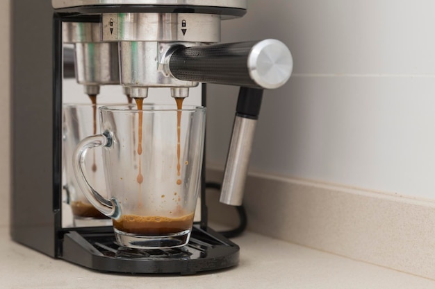 Photo la cafetière à espresso fait du café les jets de café tombent sur la tasse de verre la cafetière maison