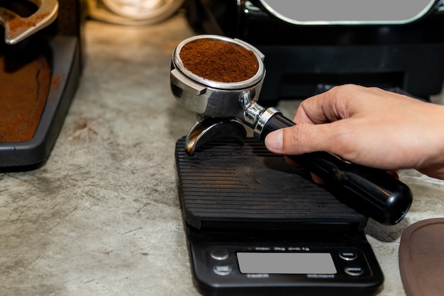 La cafetière est en train de peser le café torréfié qui a été broyé afin d'obtenir le fond selon la recette