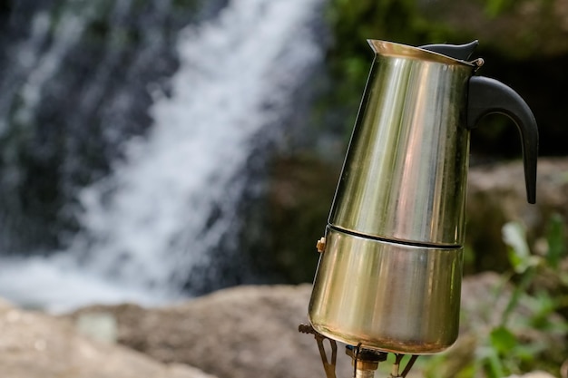 Cafetière manuelle au bord d'une cascade faisant du café