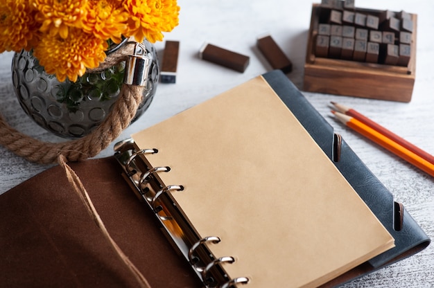 Cahier artisanal ouvert vide et fleurs de chrysanthème orange sur table rustique.