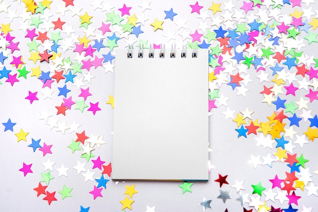 Cahier blanc sur fond blanc avec des étoiles scintillantes multicolores éparses Place pour le texte