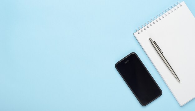Cahier blanc avec un stylo en métal et un téléphone.