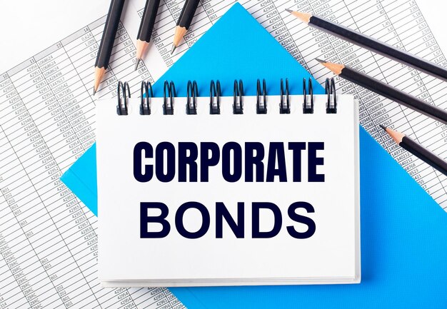 Cahier blanc avec le texte CORPORATE BONDS sur la table à côté de crayons noirs sur fond bleu et de rapports. Concept d'entreprise