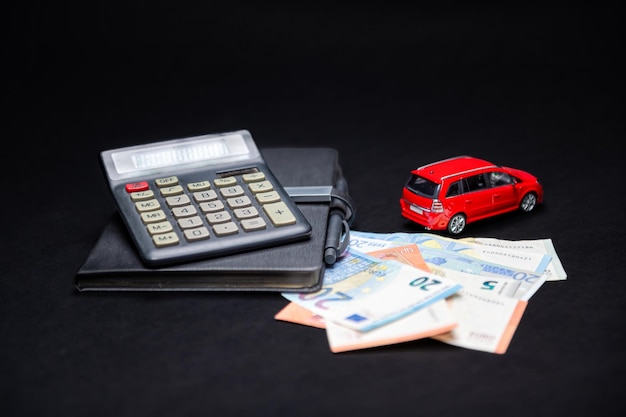 Cahier de calculatrice de billets en euros et voiture jouet rouge sur fond noir concept d'assurance et de prêt