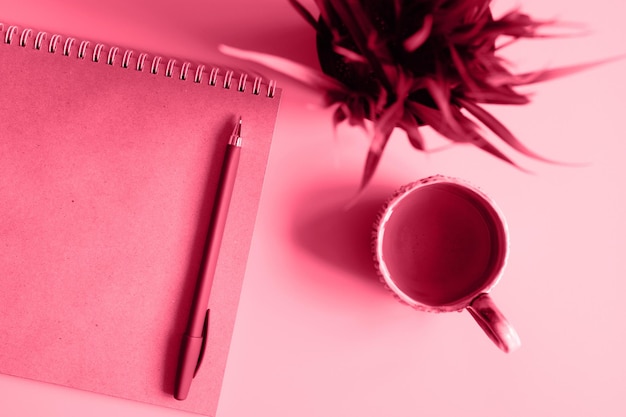 Cahier ou carnet de croquis en papier kraft et un stylo et une tasse de thé et une plante sur fond rose dans les tons de couleur tendance viva magenta de l'année 2023