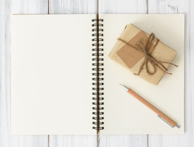 Cahier, crayon brun et boîte-cadeau pacel sur table en bois blanc, mise à plat