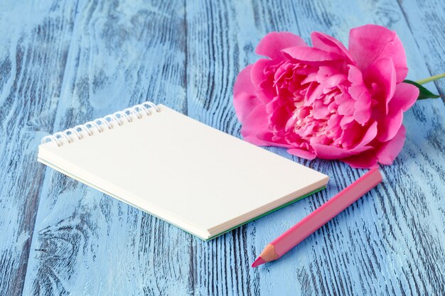 Photo cahier avec un crayon et des fleurs de pivoines sur le bois