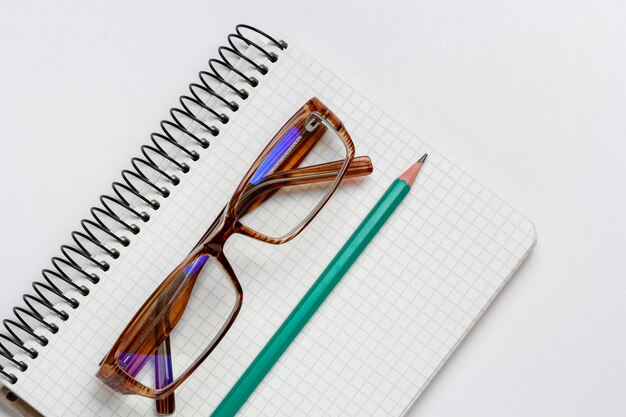 cahier, crayon et lunettes sur fond blanc isolé