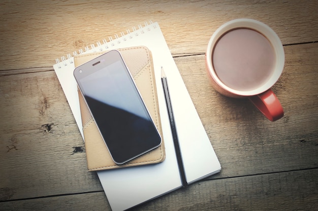 Cahier avec crayon, téléphone intelligent et tasse de café sur fond de bois