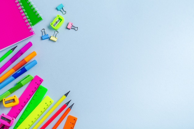 Cahier, crayons de couleur, règle, stylo, gomme, taille-crayon et papeterie scolaire et de bureau sur fond bleu.