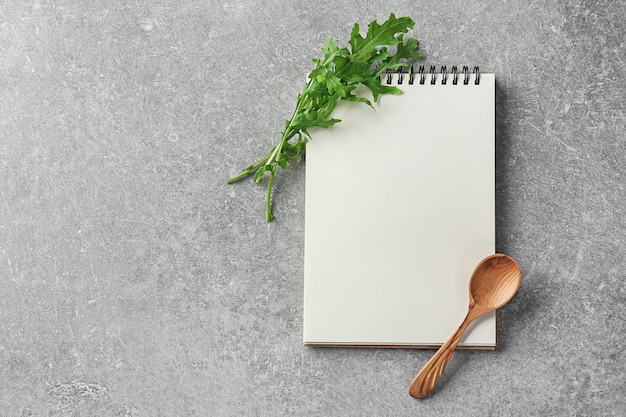 Cahier avec cuillère en bois et roquette sur fond gris Cours de maître de cuisine