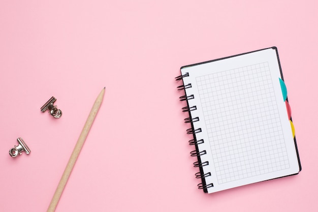 Cahier dans une cage avec un crayon sur fond rose