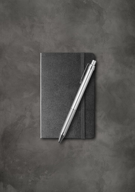 Cahier fermé noir avec un stylo. isolé sur fond de béton foncé