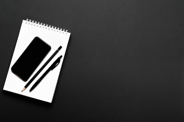 Cahier ouvert blanc avec crayon noir, stylo et smartphone. Bureau, papeterie