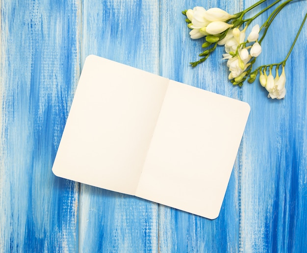 Cahier ouvert et fleur de freesia sur fond bleu en bois