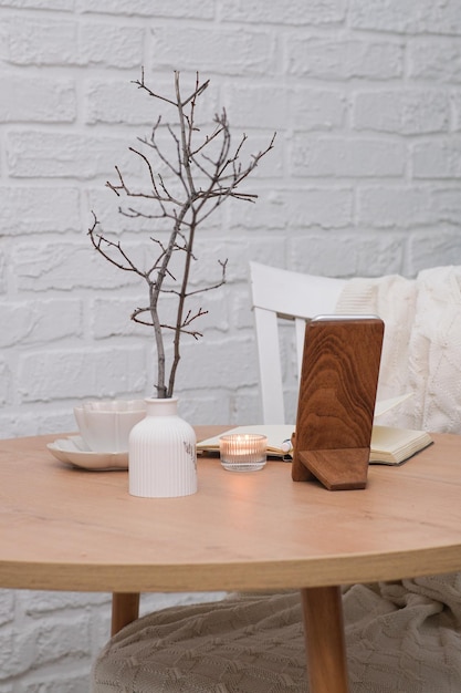 Un cahier ouvert avec un stylo blanc une tasse de thé une bougie allumée un vase avec des branches sur une table en bois et