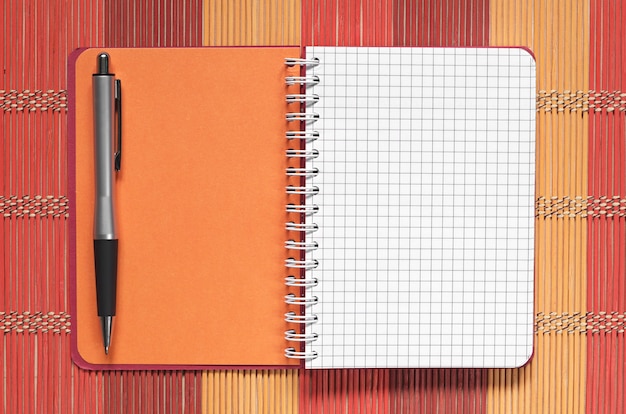 Photo cahier ouvert avec un stylo sur une serviette en bambou colorée, vue de dessus