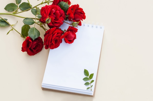 Un cahier sur un ressort sur fond beige à côté d'un bouquet de roses rouges