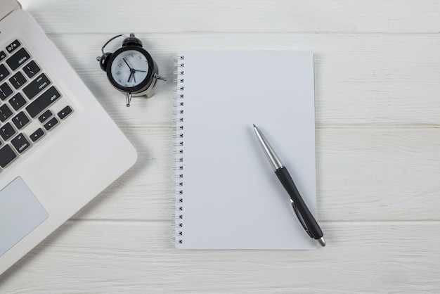 Un cahier vide avec un stylo se trouve au-dessus d'une table de bureau en bois avec un ordinateur portable et des fournitures Vue de dessus avec espace de copie à plat