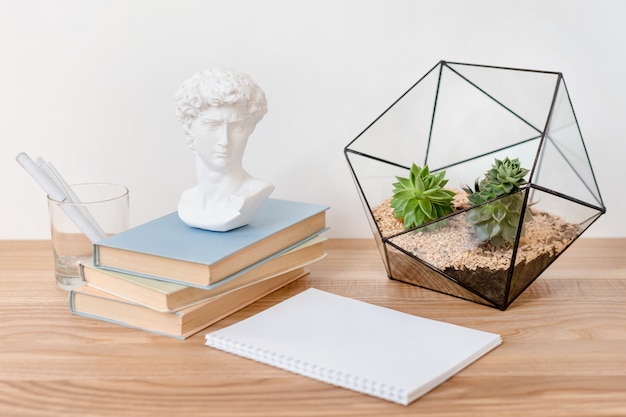 Cahier vide sur table en bois avec des livres, des plantes succulentes et une petite sculpture en plâtre de David