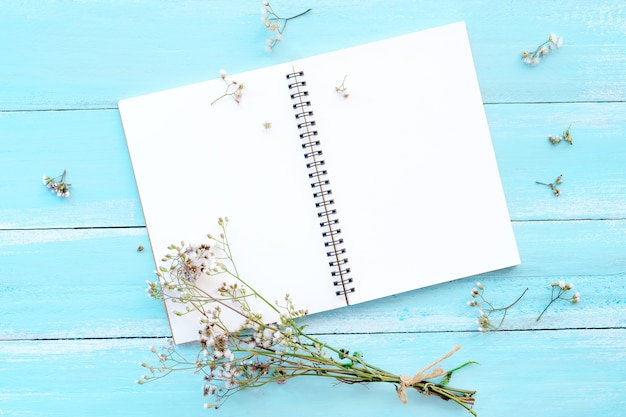 Cahier vierge et bouquet de fleurs sauvages sur un fond en bois bleu.