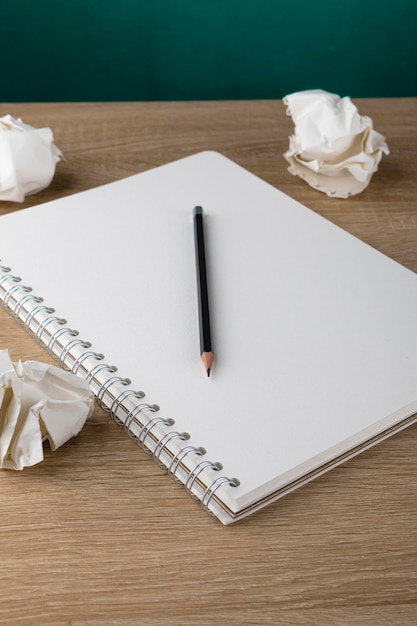 Un cahier vierge avec un crayon sur une table en bois et des boules de papier froissées sans idées.