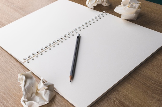 Photo un cahier vierge avec un crayon sur une table en bois et des boules de papier froissées sans idées.