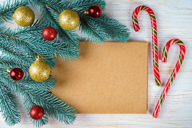 Cahier vierge avec décoration de Noël. Branches d'arbres de Noël avec des boules rouges et dorées et deux bonbons avec espace de copie sur fond de bois blanc