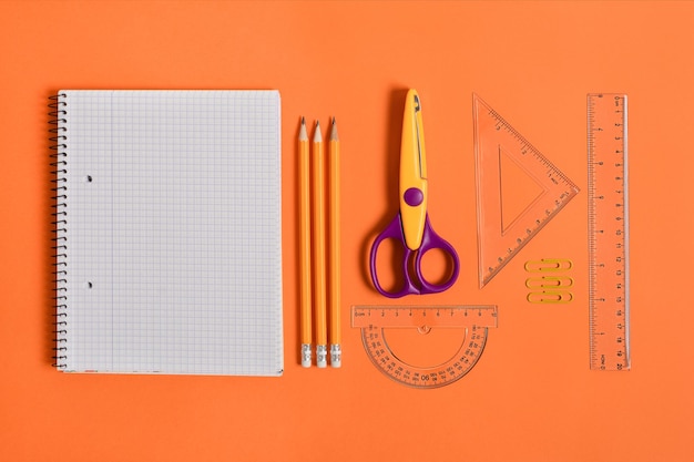 Cahier vierge avec fournitures scolaires et de bureau sur la vue de dessus de fond orange