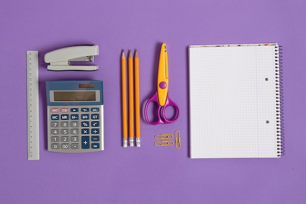 Cahier vierge avec fournitures scolaires et de bureau sur la vue de dessus de fond violet