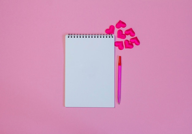 Un cahier vierge ouvert sur fond rose avec des coeurs.