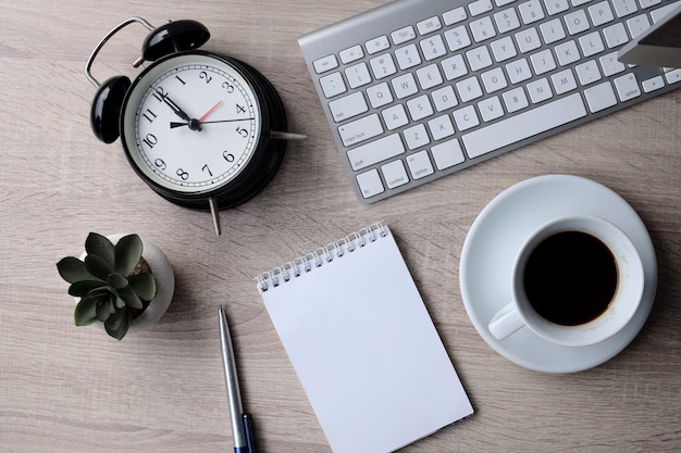 Cahier vierge avec réveil et café sur le bureau.