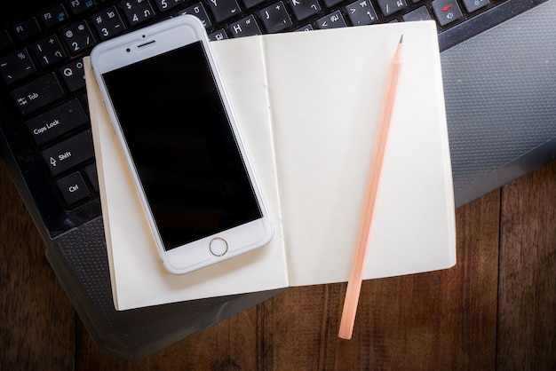 Cahier vierge et smartphone avec un crayon sur un ordinateur portable