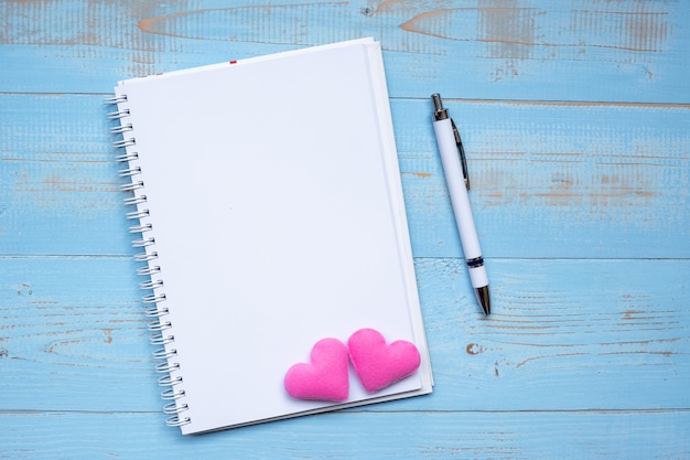 Cahier vierge et stylo avec une décoration de couple coeur rose sur une table en bois bleue