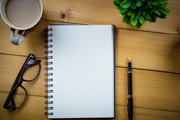 Cahier vierge avec stylo et lunettes à côté de la tasse de café sur la table en bois