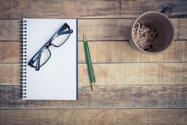 Cahier vierge avec stylo et lunettes sur fond de bois