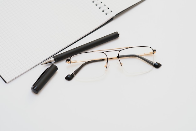 Un cahier vierge avec un stylo se trouve sur une table de bureau blanche. Vue de dessus avec espace de copie, mise à plat.