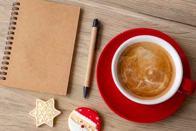 Cahier vierge, tasse à café noire, biscuits de Noël et stylo sur table en bois, vue de dessus et espace de copie. Noël, bonne année, objectifs, résolution, liste de tâches, concept de stratégie et de plan