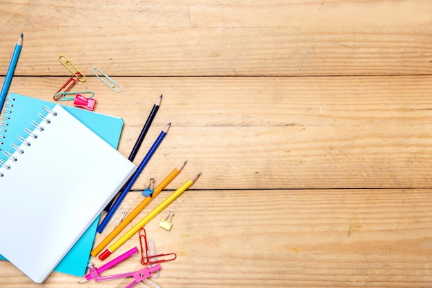 Cahiers avec fournitures scolaires et papeterie sur le fond de la table en bois