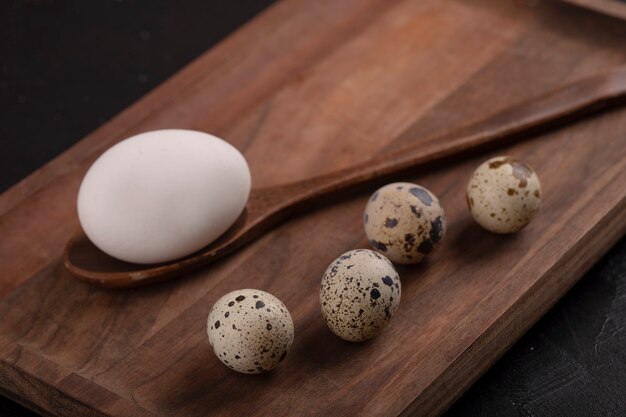 Caille bio non cuite et œufs de poule sur une planche à découper en bois.