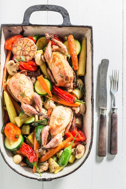 Cailles rôties aux légumes en cocotte sur fond blanc