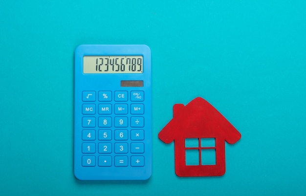 Calcul du coût du logement locatif. Figurine de maison rouge, calculatrice sur fond bleu. Vue de dessus