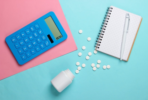 Calcul du coût des frais médicaux. Calculatrice, cahier et bouteille de pilules sur fond bleu rose. Vue de dessus. Minimalisme