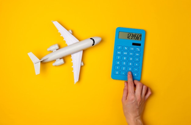 Calcul Du Coût Des Voyages Aériens, Voyages. Main Appuyez Sur Le Bouton De La Calculatrice Bleue Et Figurine D'avion De Passagers Sur Jaune