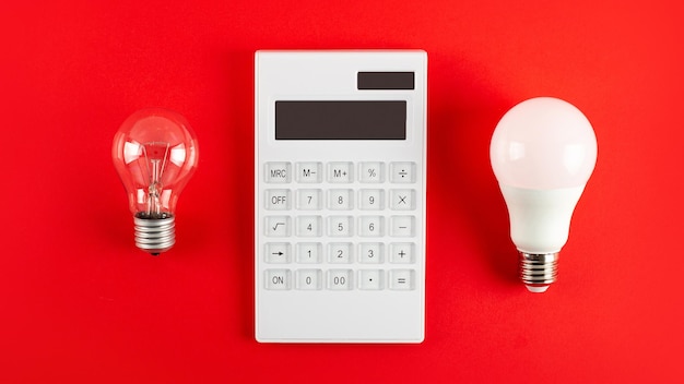 Calculatrice blanche et lampe à incandescence ou ampoule LED sur fond rouge Concept montrant le paiement